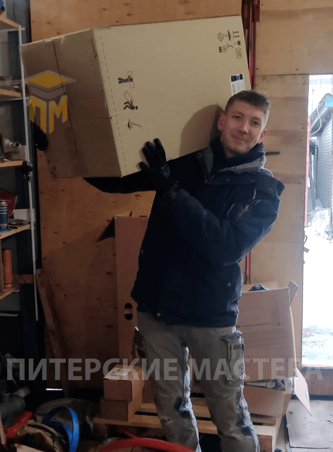 Сотрудник компании "Питерские мастера" с коробкой оборудования на складе. Подготовка к доставке материалов и оборудования для монтажа системы отопления.